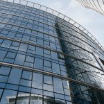 Captured from below, this image showcases a modern glass skyscraper reflecting the sky, located in Warsaw.