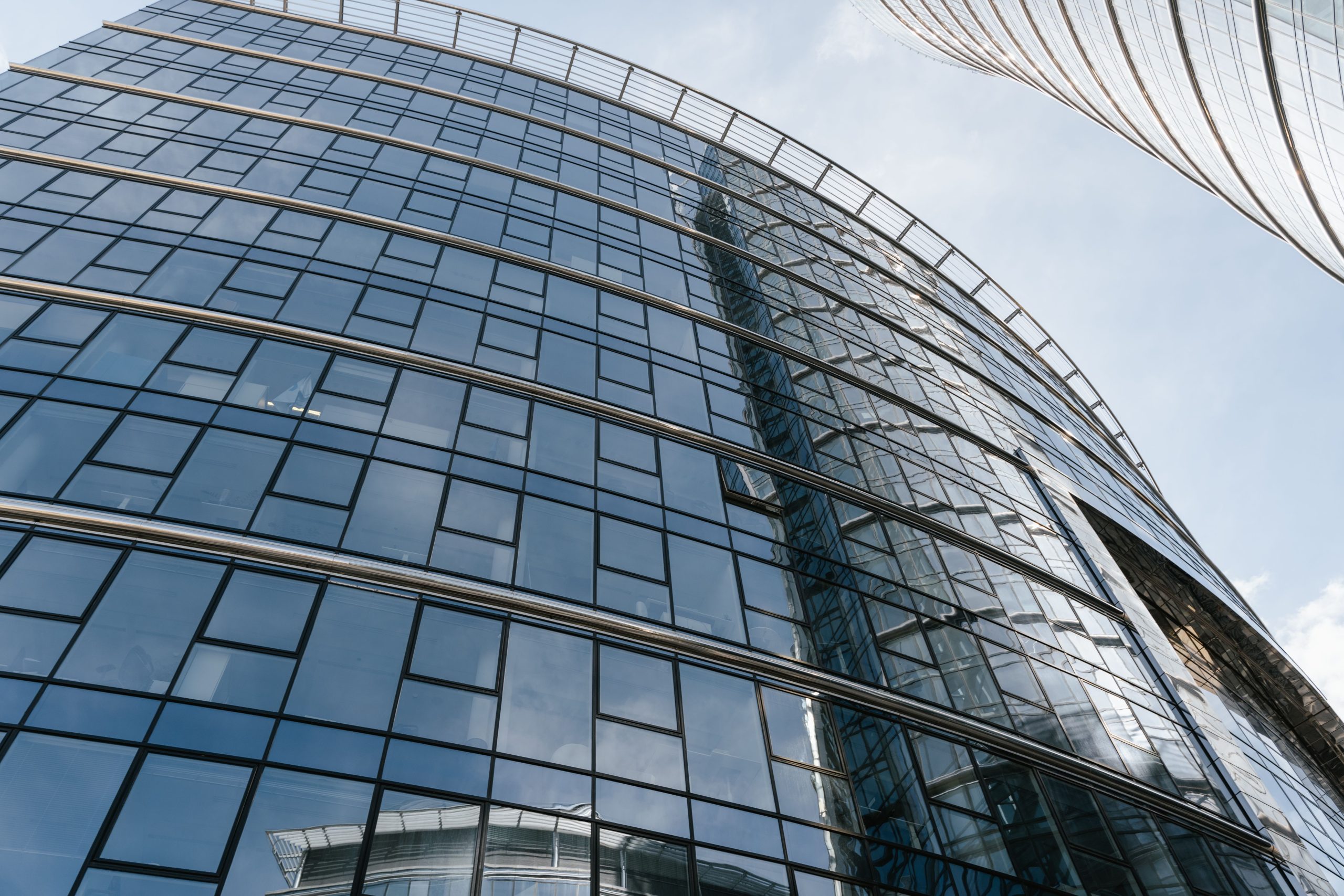 Captured from below, this image showcases a modern glass skyscraper reflecting the sky, located in Warsaw.