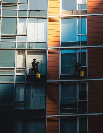 Two workers hanging to clean windows on a modern skyscraper facade.